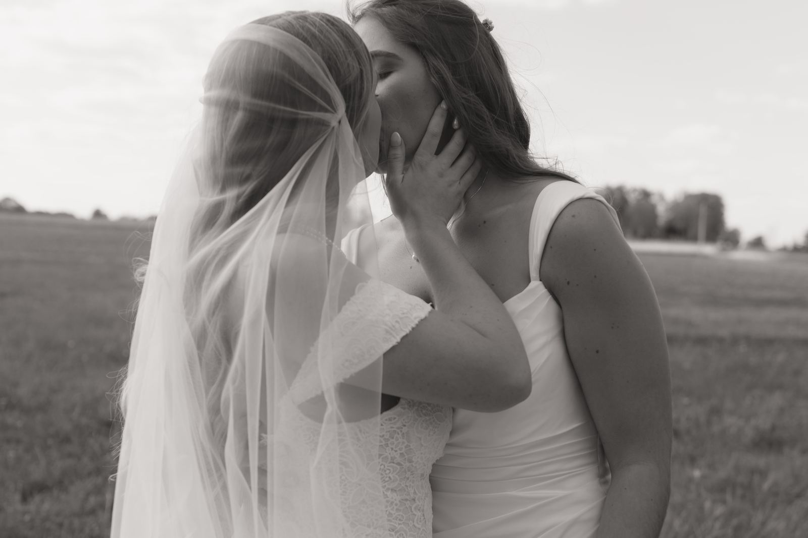 Two brides sharing a kiss beneath a flowing veil