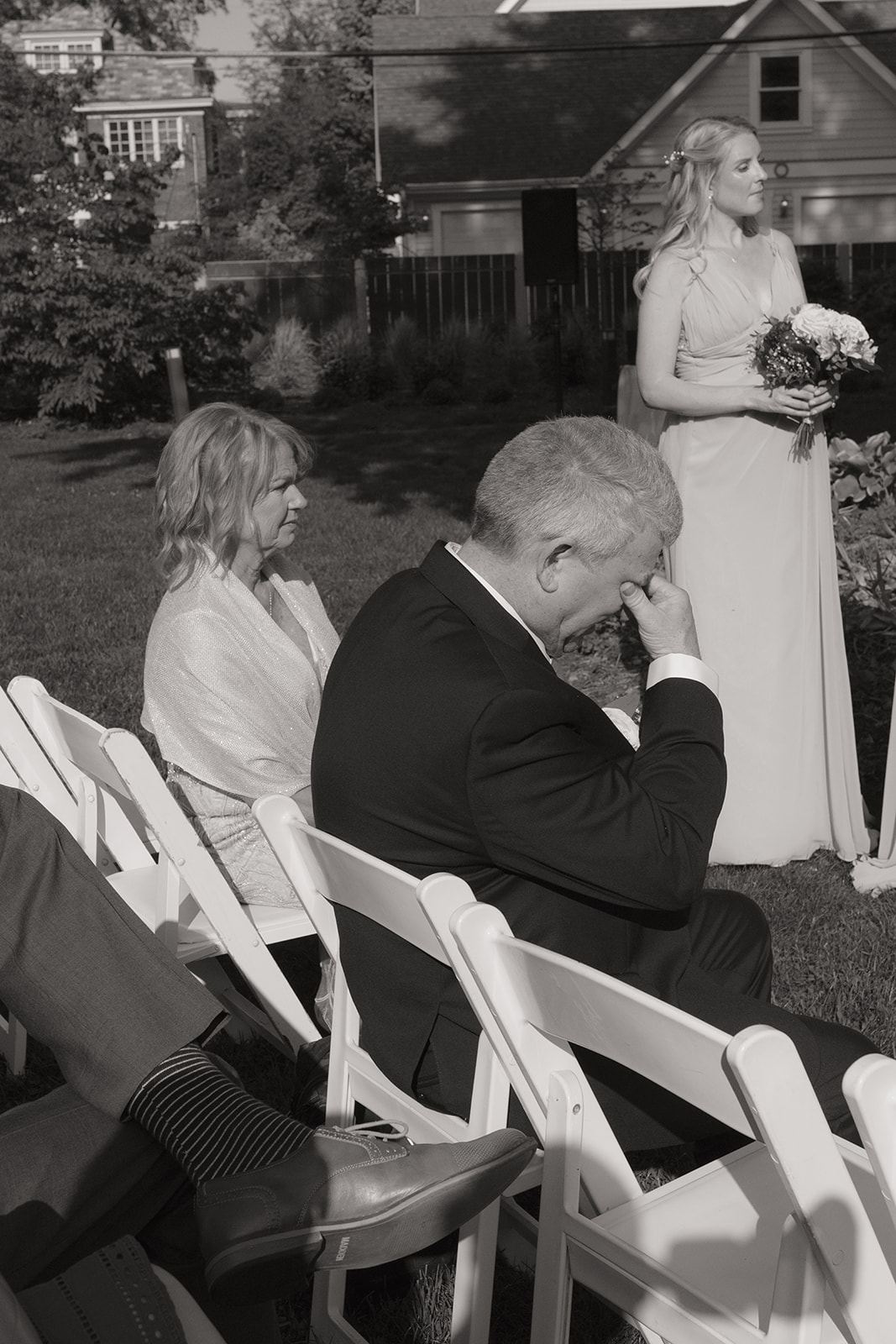 Man in a suit wiping away tears during an outdoor garden ceremony