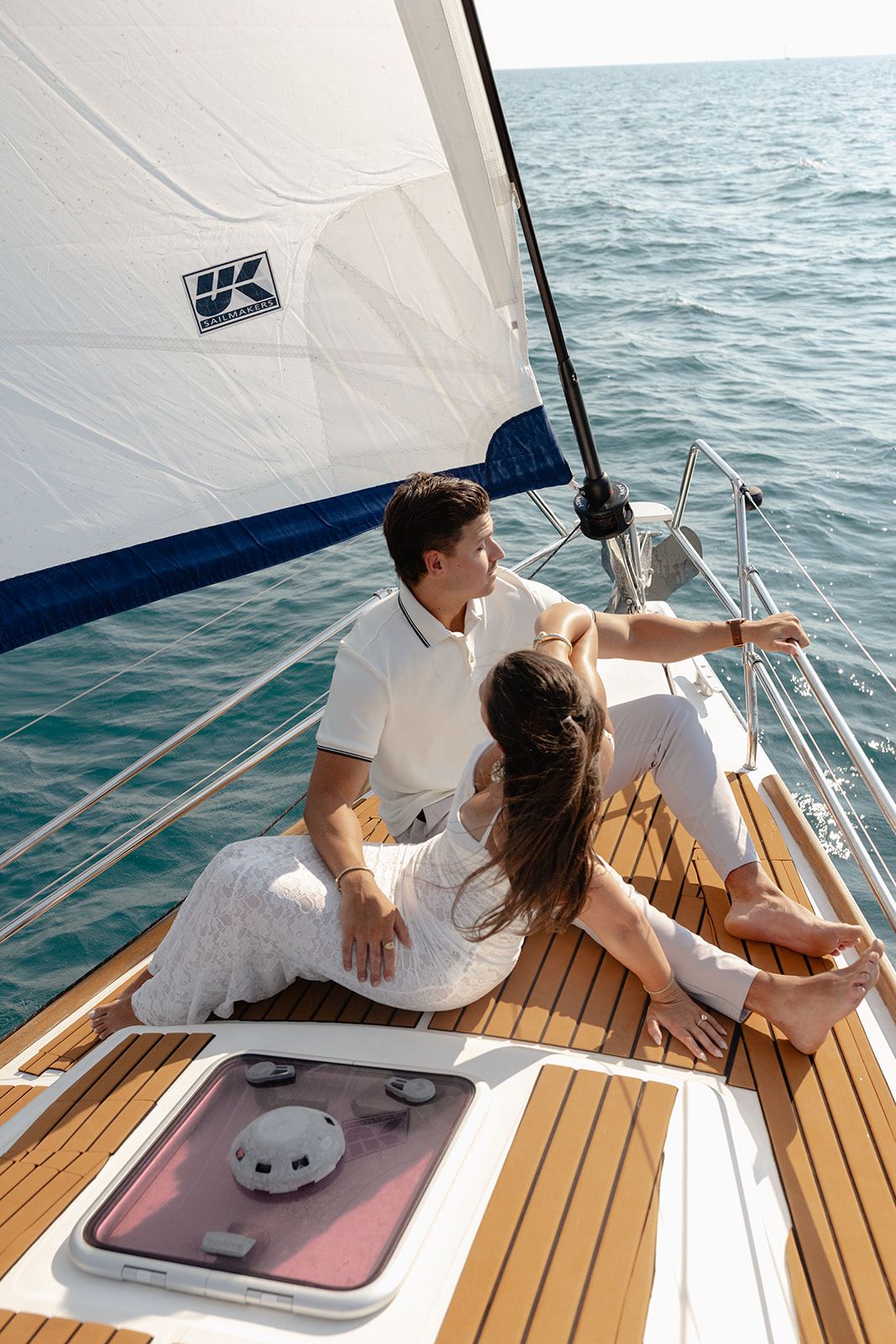 Couple dressed in white relaxing together on the bow of a sailboat