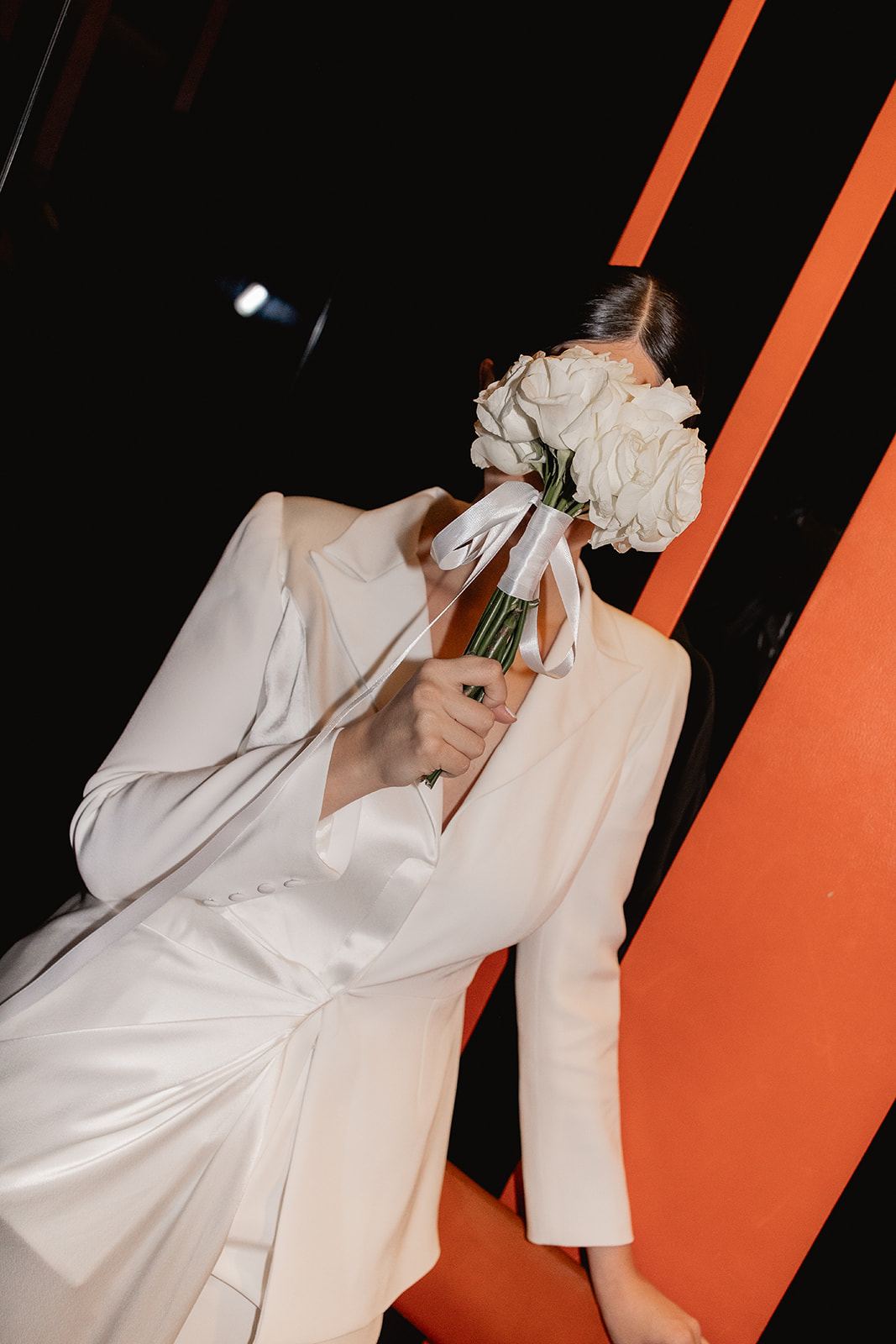 Bride in a white suit hiding her face behind a bouquet of white roses