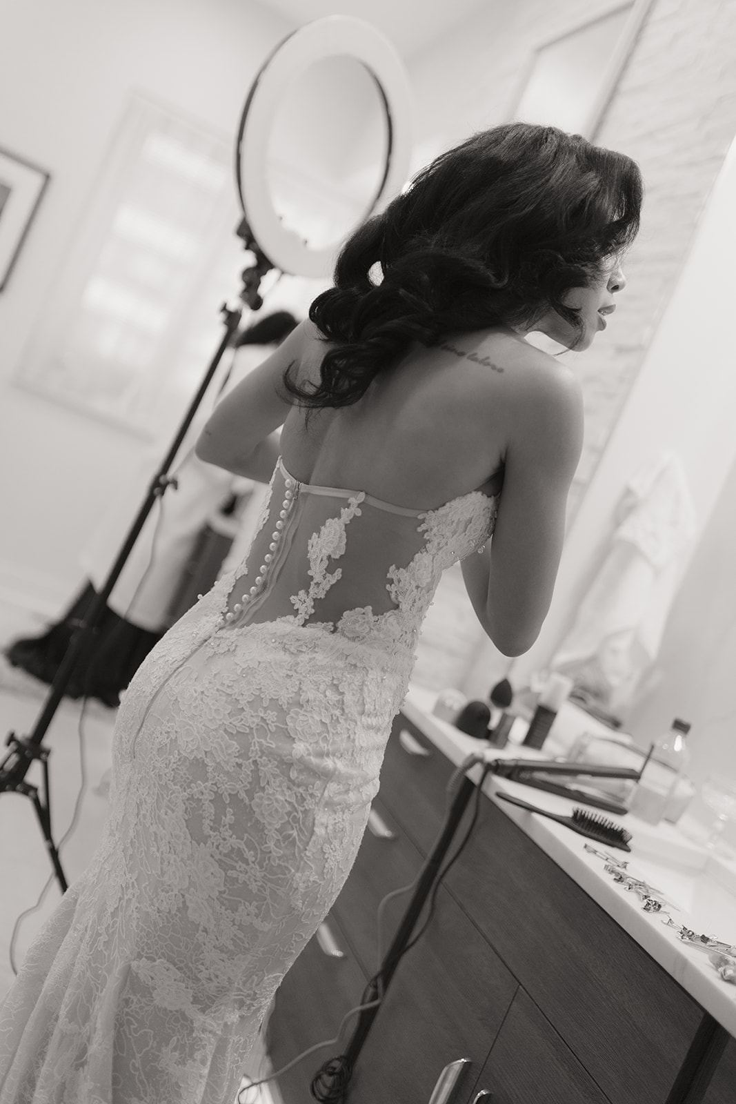 Bride in a lace gown with a sheer back getting ready at a vanity