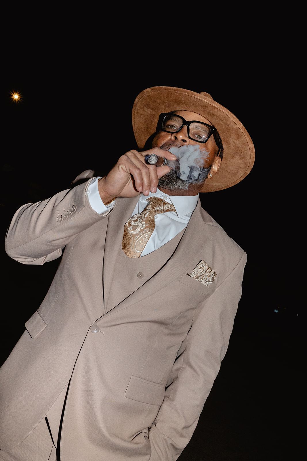 Guest in a tan suit and hat smoking a cigar at night