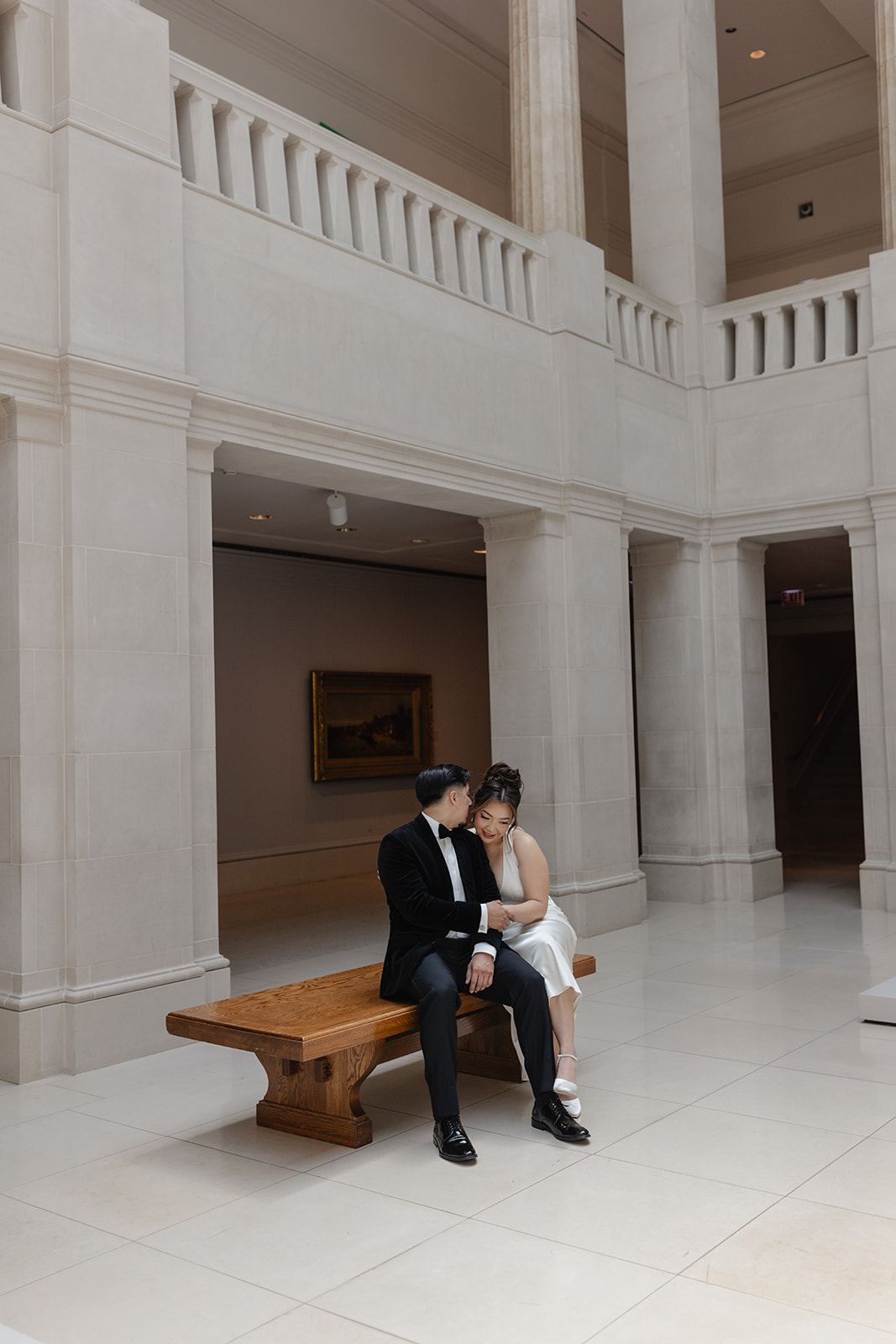 Couple seated on a wooden bench in a bright museum hall with balconies