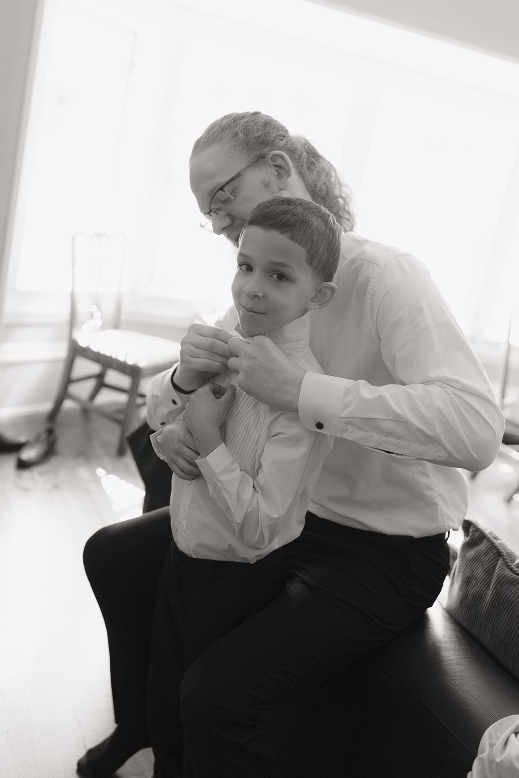 Man adjusting a young boy's collar while getting ready, black and white